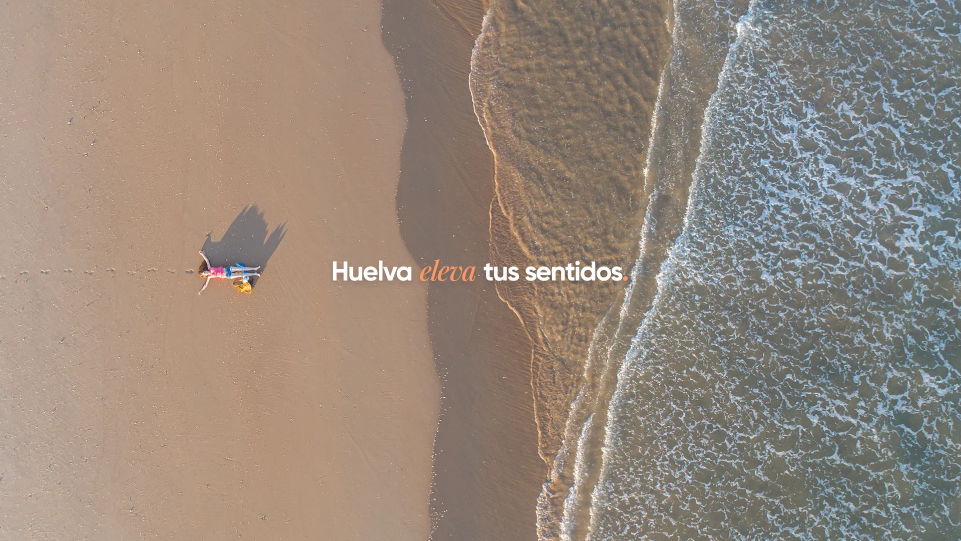 Eslogan «Huelva eleva tus sentidos» sobre una vista aérea de la playa