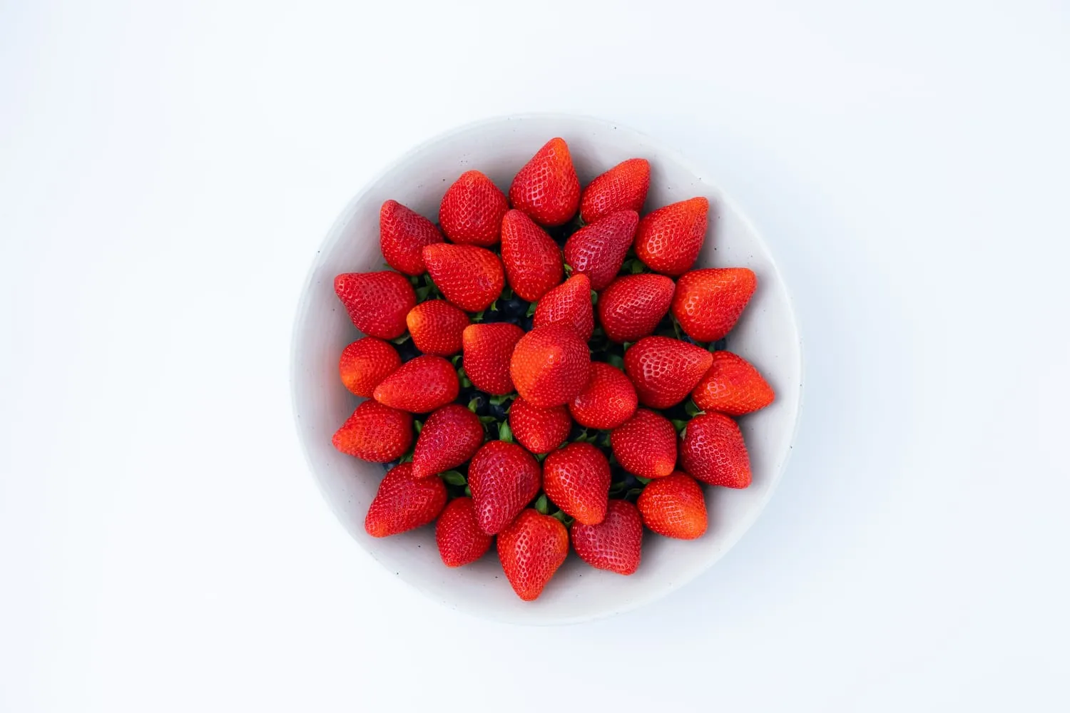 Bol blanco lleno de fresas, fotografiado cenital sobre fondo blanco de estudio