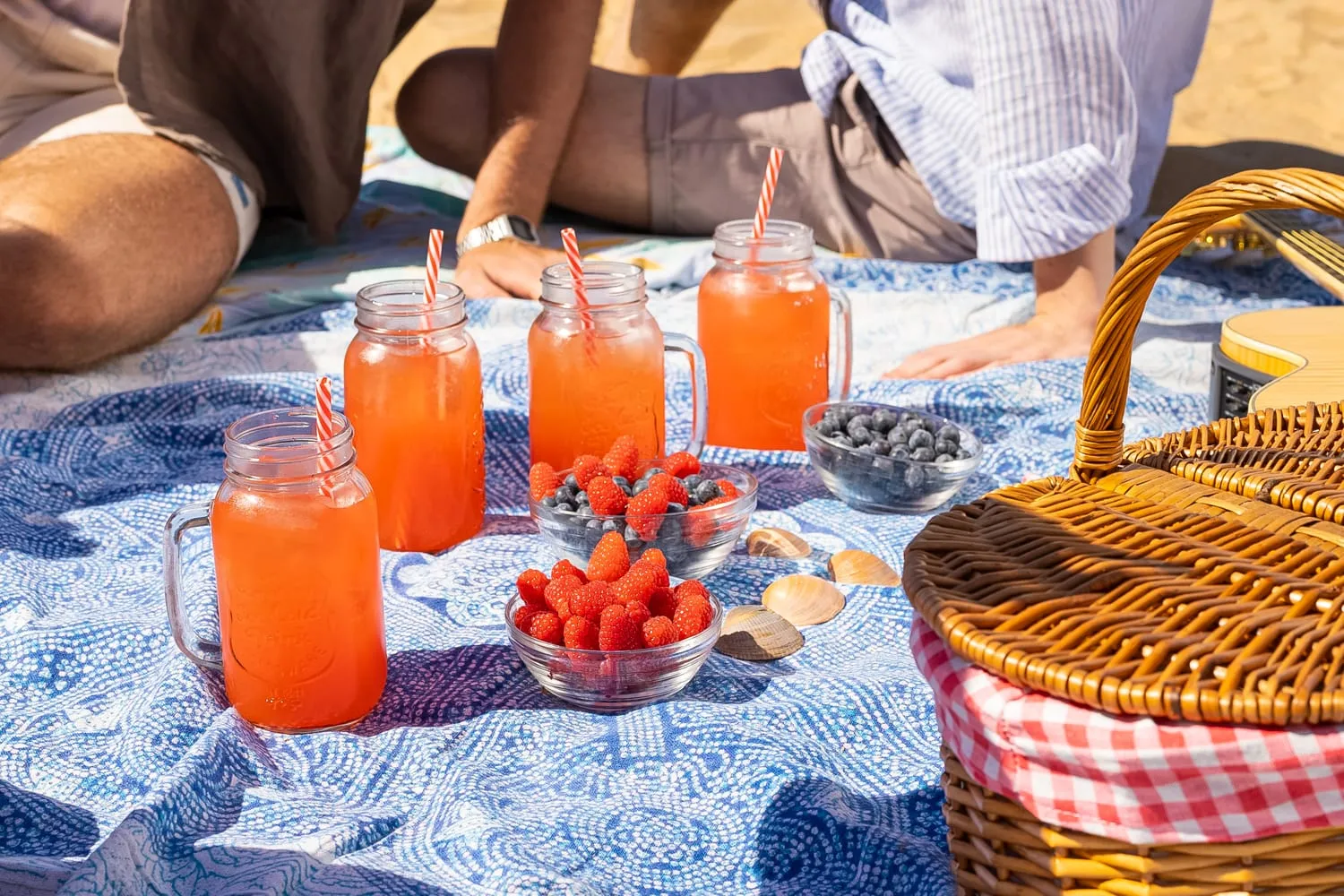 Bebidas de frutos rojos y un cesto de pícnic sobre una manta en la playa