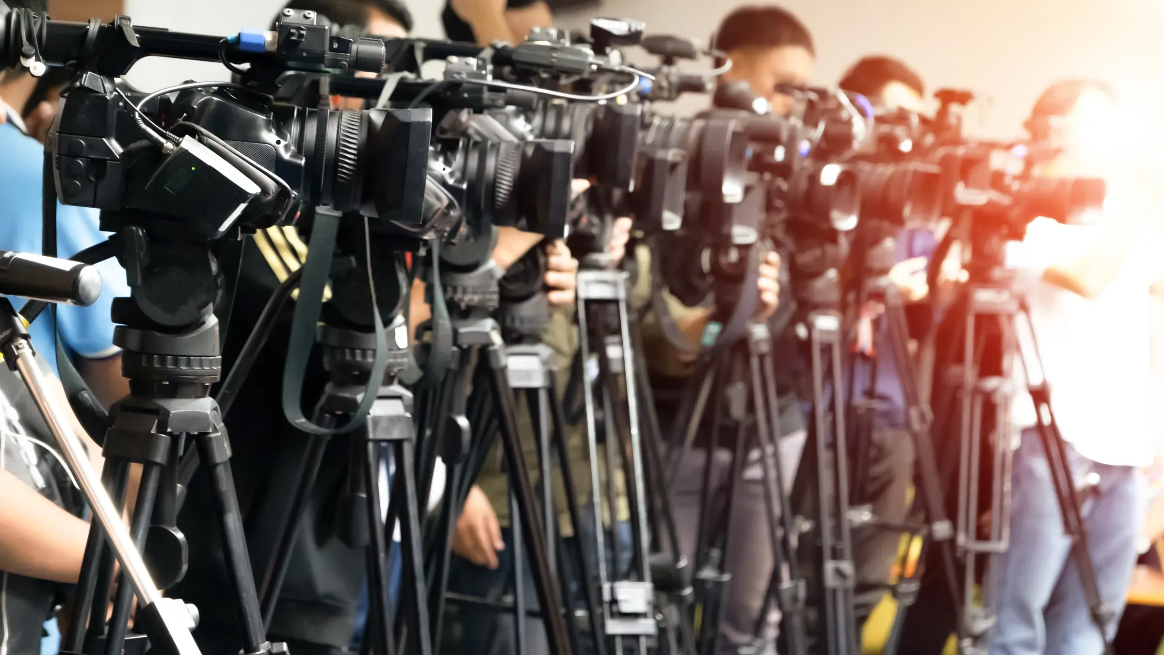 Una hilera de cámaras de televisión sobre trípodes cubriendo un acto.
